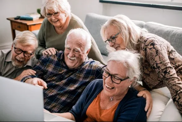 A group of older adults laughing around a laptop