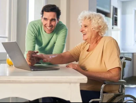 A Wizard helping an older woman with a laptop at her kitchen table